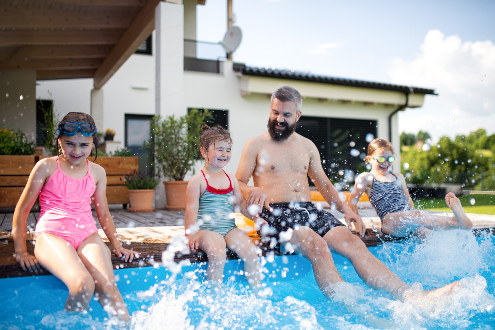Family Splashing in a Backyard Vinyl Pool - Barr Pool Builders Northern Utah Father and three young daughters laughing and splashing at the edge of a backyard swimming pool built by Barr Pool Builders in Northern Utah