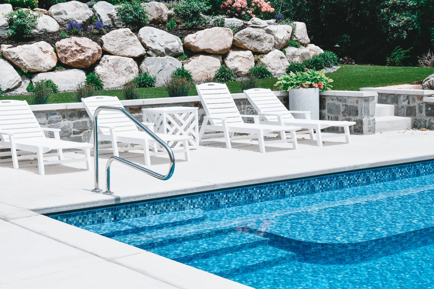 Blue mosaic-tile inground vinyl swimming pool with poolside lounge chairs and boulder wall in Kaysville, Utah by Barr Pool Builders