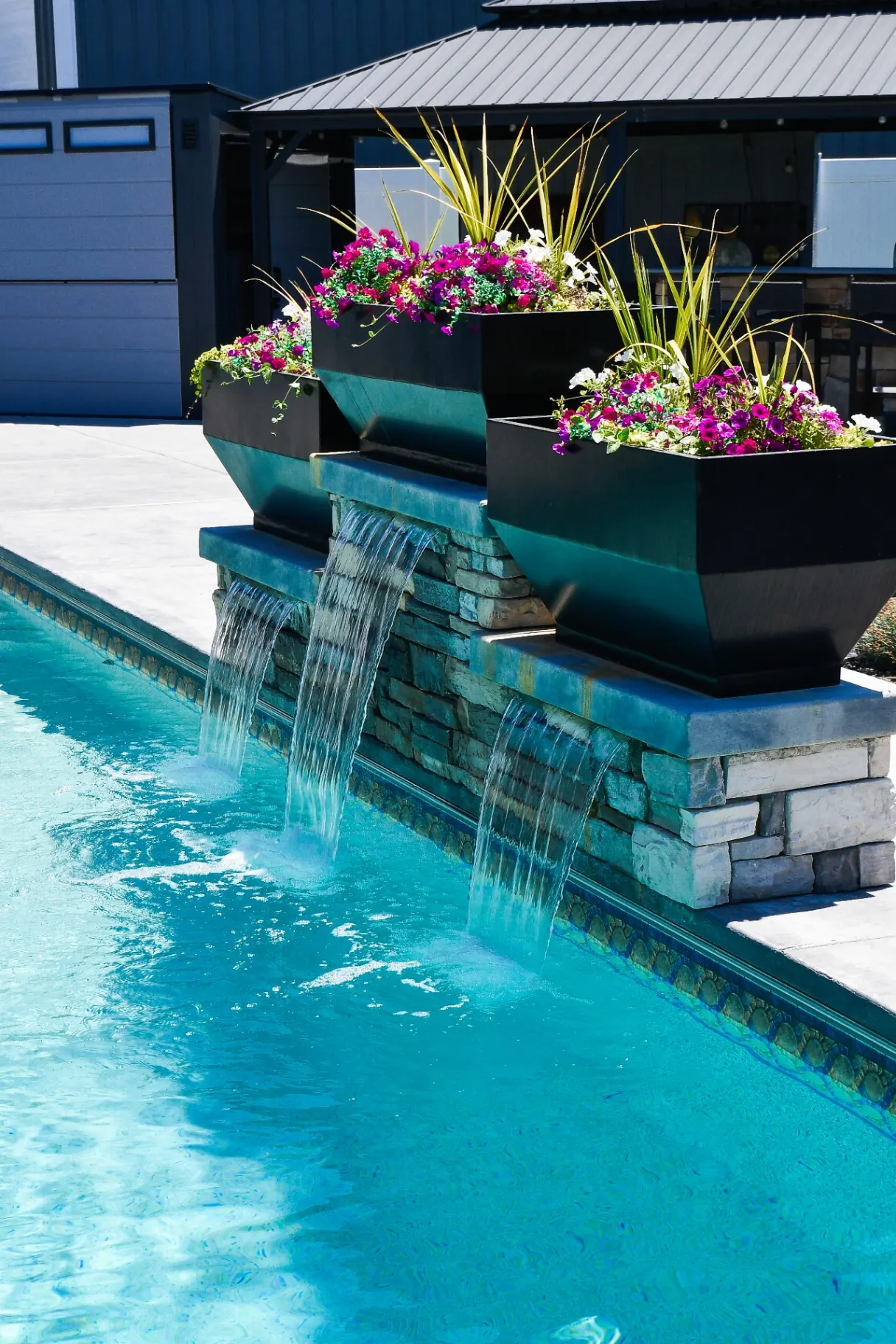 Syracuse Utah Vinyl Pool with Stone Waterfall Feature - Barr Pool Builders Custom vinyl swimming pool with tiered stone waterfall feature and floral planters in a Syracuse, Utah backyard by Barr Pool Builders