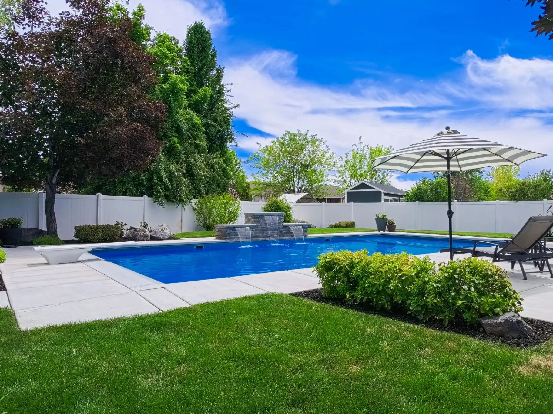 Layton Utah Backyard Vinyl Pool with Water Feature - Barr Pool Builders Backyard vinyl inground swimming pool with stone water feature, diving board and umbrella lounge in Layton, Utah by Barr Pool Builders