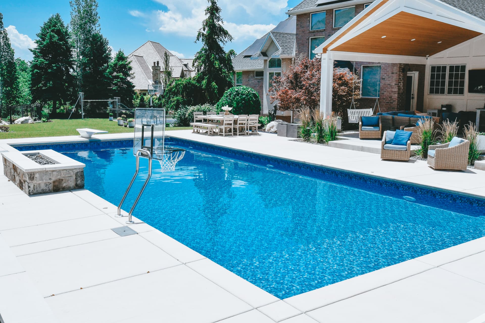 Farmington Utah Luxury Vinyl Pool with Basketball, Firepit & Pavilion - Barr Pool Builders Luxury vinyl inground swimming pool with in-pool basketball hoop, stone firepit, diving board and covered pavilion lounge in a Farmington, Utah estate by Barr Pool Builders