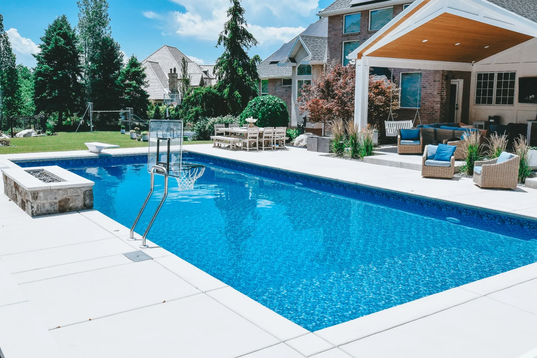 Luxury vinyl swimming pool with in-pool basketball hoop, diving board and stone firepit in a Layton, Utah backyard built by Barr Pool Builders